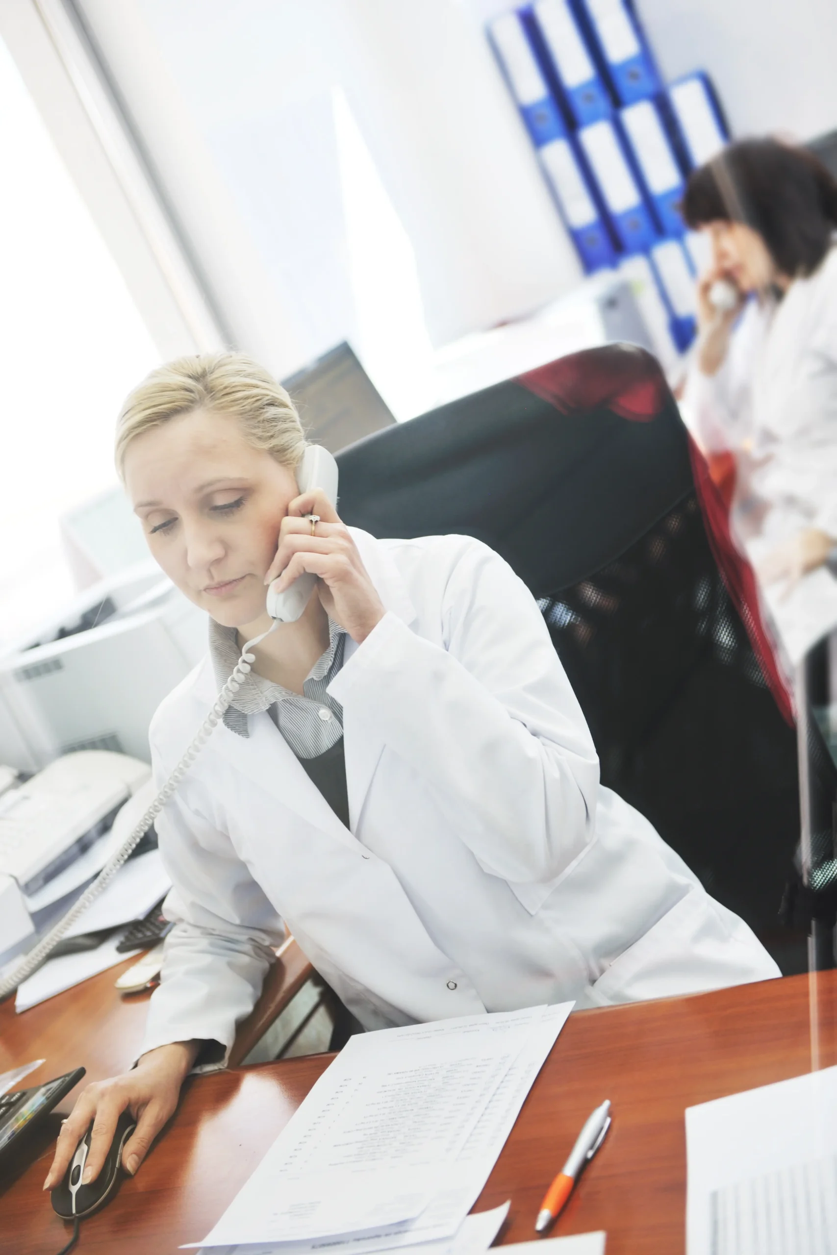 Medical professional on a phone call at a desk.